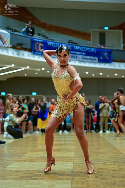Dancesport competitor: Female dancer in foreground: champagne-colored Latin dance dress heavily embelli