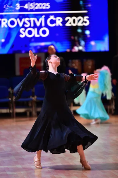 Dancesport competitor: Female dancer in foreground: black ballgown with long, sheer sleeves and a volum