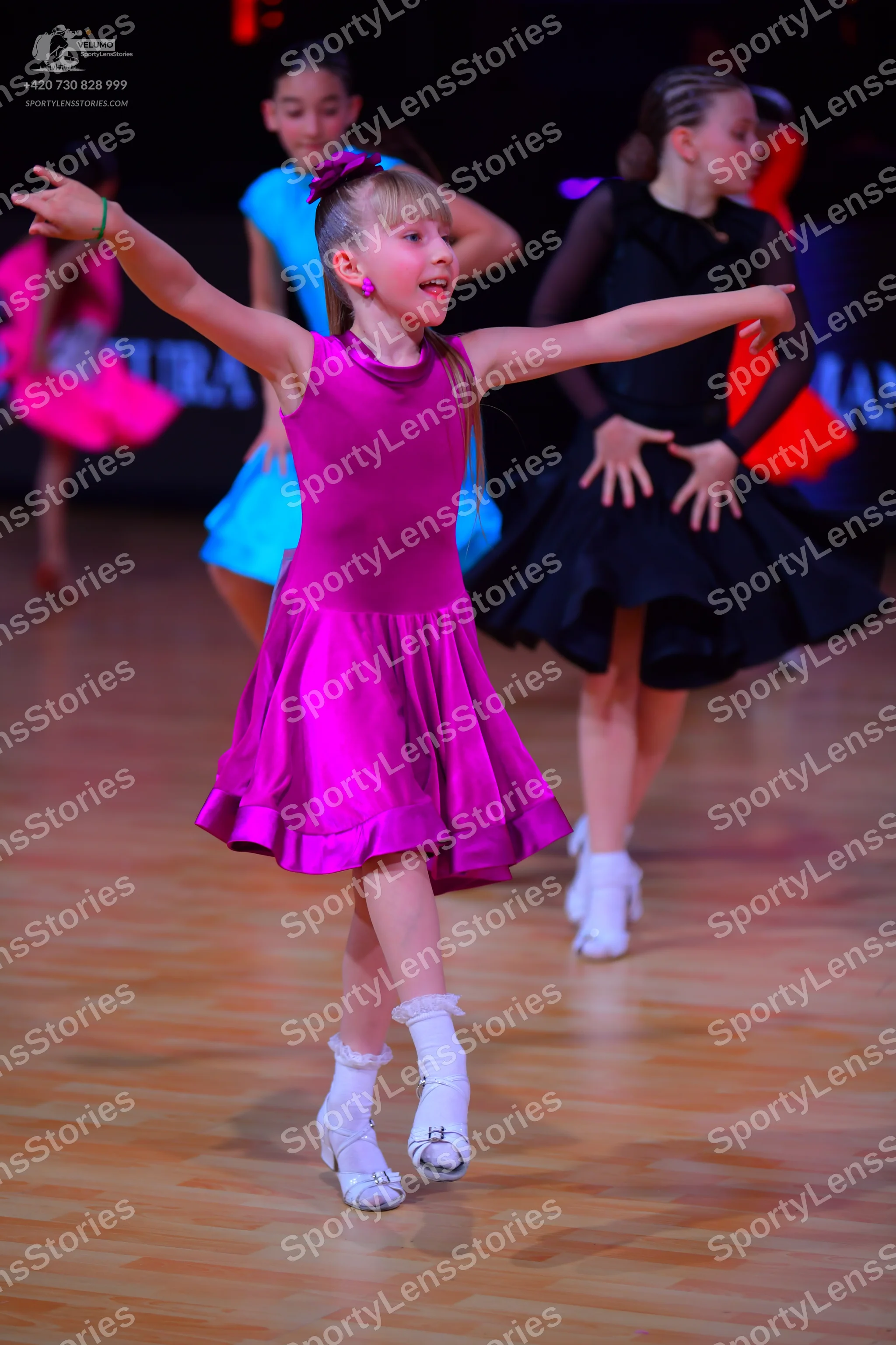Dancesport competitor: Female dancer in foreground: magenta satin sleeveless dress with a high neckline