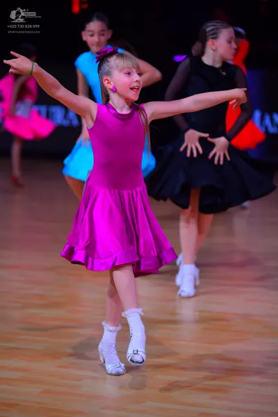 Dancesport competitor: Female dancer in foreground: magenta satin sleeveless dress with a high neckline