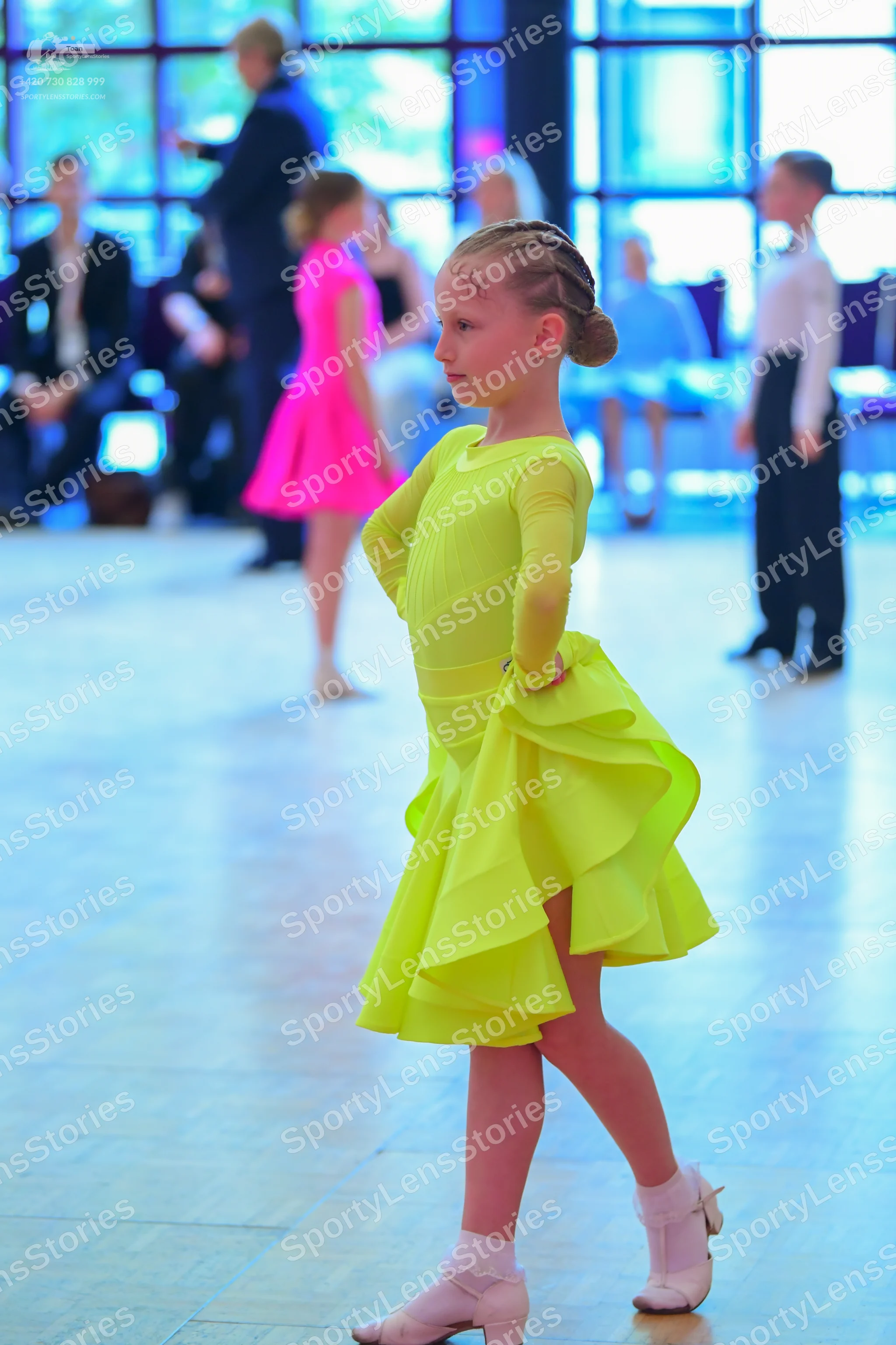 Dancesport competitor: Female dancer in foreground: neon yellow long-sleeved latin dress with a ruffled