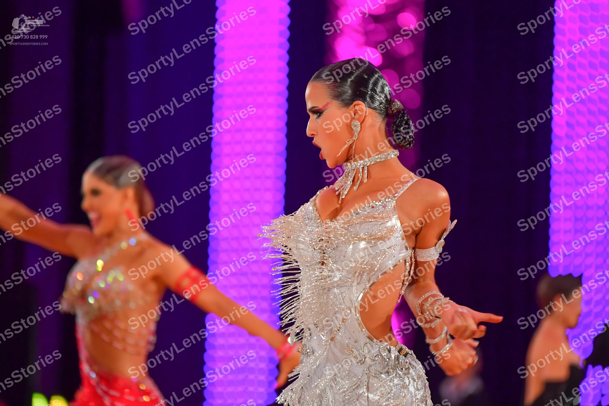 Dancesport competitor: Female dancer in foreground: silver Latin dress with sequins, fringe, and side c