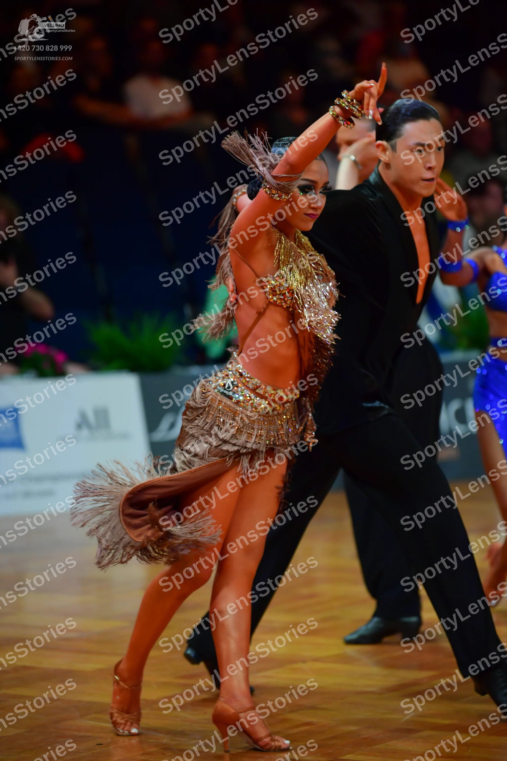 Dancesport competitor: Female dancer in foreground: gold/bronze latin dress with sequins and long fring
