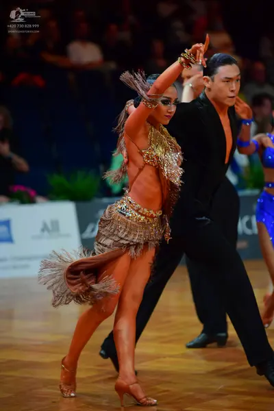 Dancesport competitor: Female dancer in foreground: gold/bronze latin dress with sequins and long fring