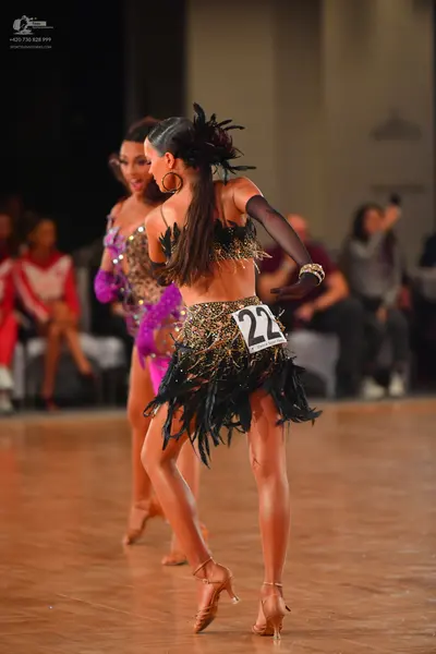 Dancesport competitor #22: Female dancer in foreground: black and gold sequin Latin dress with a feathered/