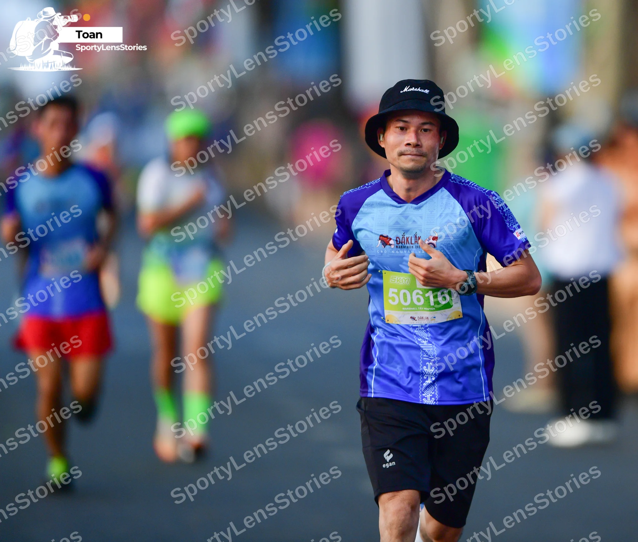 Marathon runner #50616: Runner 1: blue and purple patterned jersey, black shorts, black bucket hat, blac