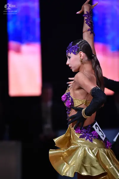 Dancesport competitor: Female dancer: gold satin Latin dance costume with purple lace floral embellishm