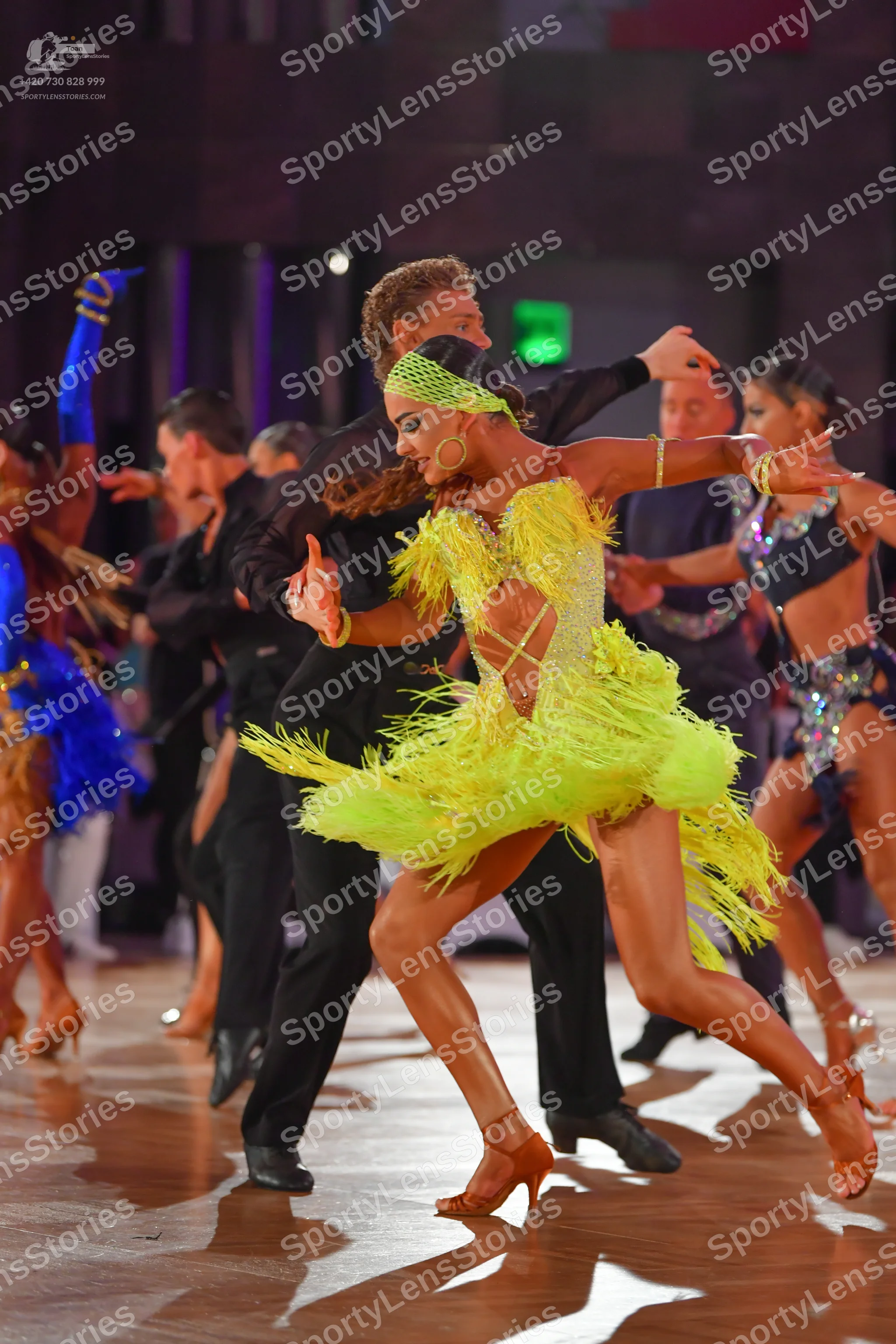 Dancesport competitor: Female dancer in center: bright yellow Latin dress with heavy fringe and a match
