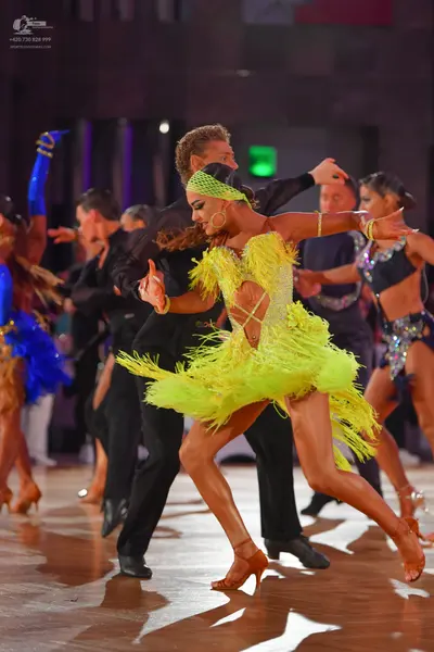 Dancesport competitor: Female dancer in center: bright yellow Latin dress with heavy fringe and a match
