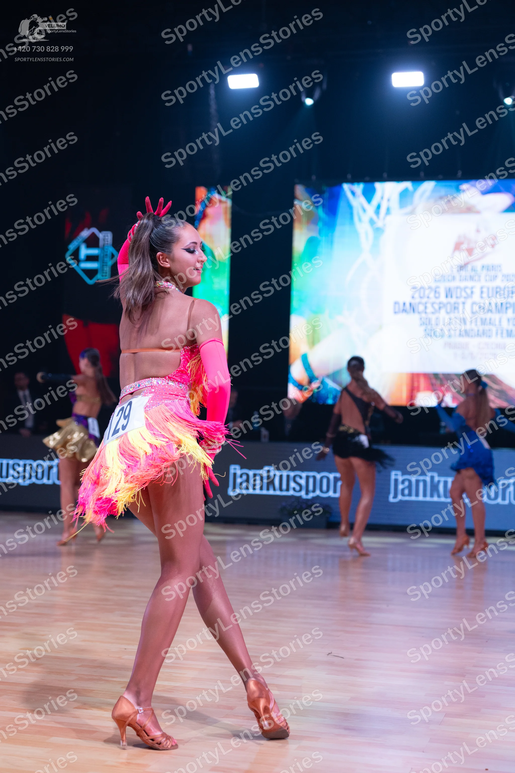 Dancesport competitor: Female dancer in foreground: pink and orange latin dress with long sleeves and p