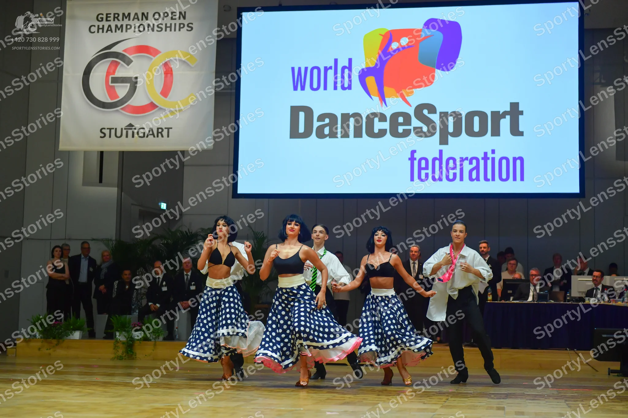 Dancesport competitor: Three female dancers: black bra-style tops and blue and white polka-dotted skirt