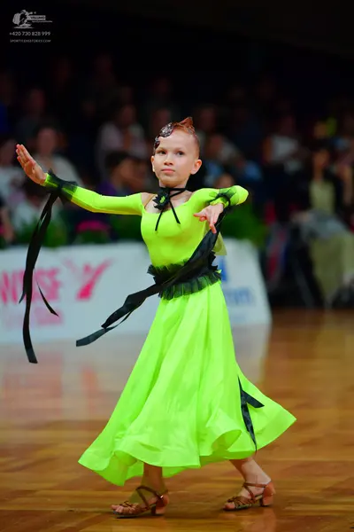 Dancesport competitor: Female dancer: neon green long-sleeved ballroom dress with black ribbon at the n