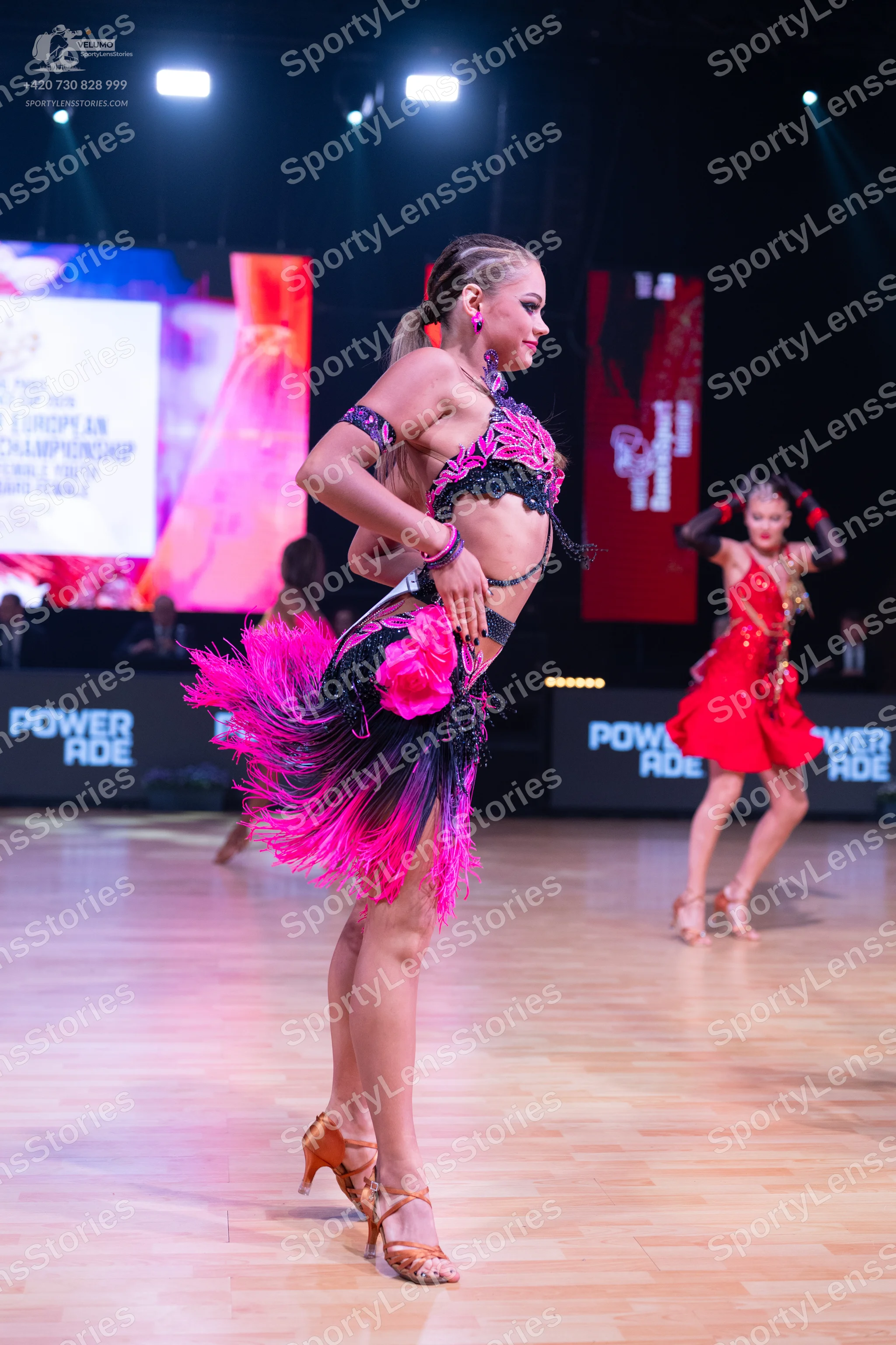 Dancesport competitor: Female dancer in foreground: pink and black latin dress with sequins, fringe, an