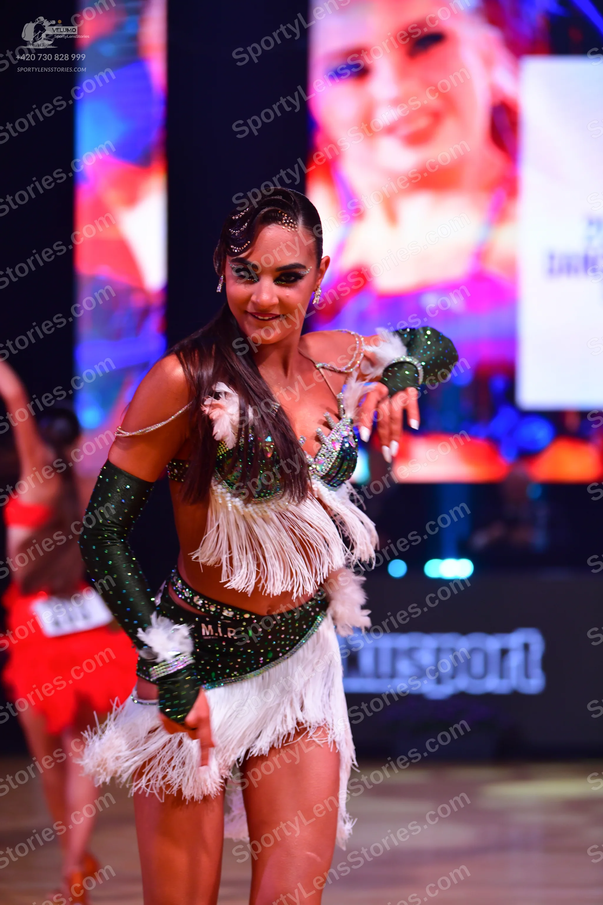 Dancesport competitor: Female dancer in foreground: green sequin latin dress with long white fringe, wh