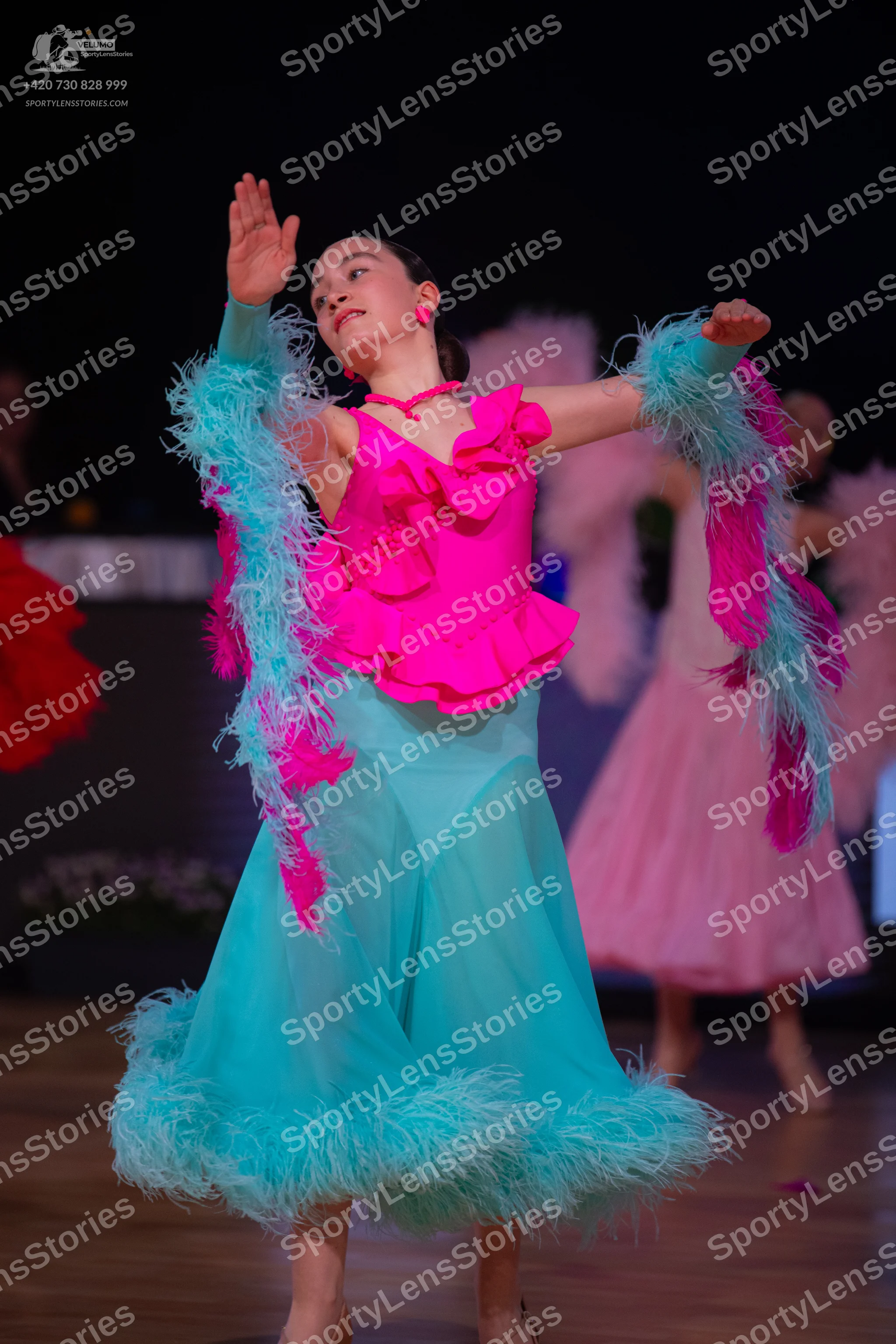 Dancesport competitor: Female dancer: bright pink ruffled Latin dress top, light blue/teal sheer skirt