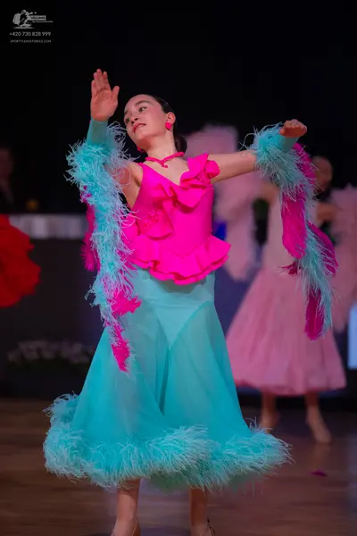 Dancesport competitor: Female dancer: bright pink ruffled Latin dress top, light blue/teal sheer skirt 