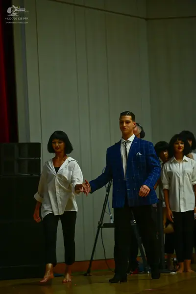 Dancesport competitor: Female dancer (left): white long-sleeved button-up shirt and black cropped trous