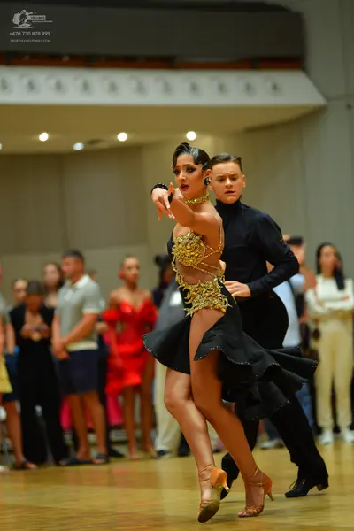 Dancesport competitor: Female dancer: black latin dress with gold sequined/beaded bodice and flared ski