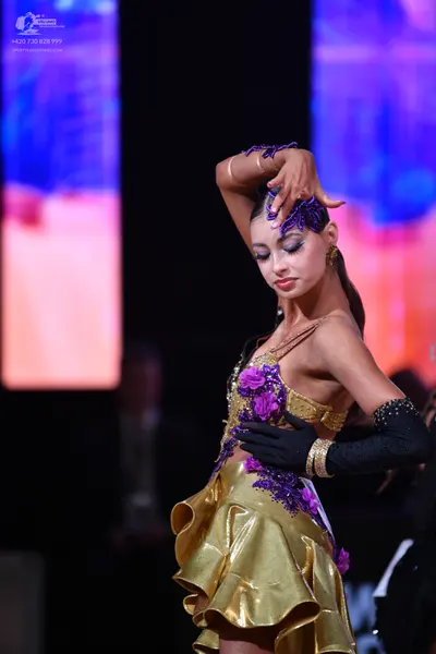 Dancesport competitor: Female dancer: gold latin dress with purple floral embellishments and a ruffled 