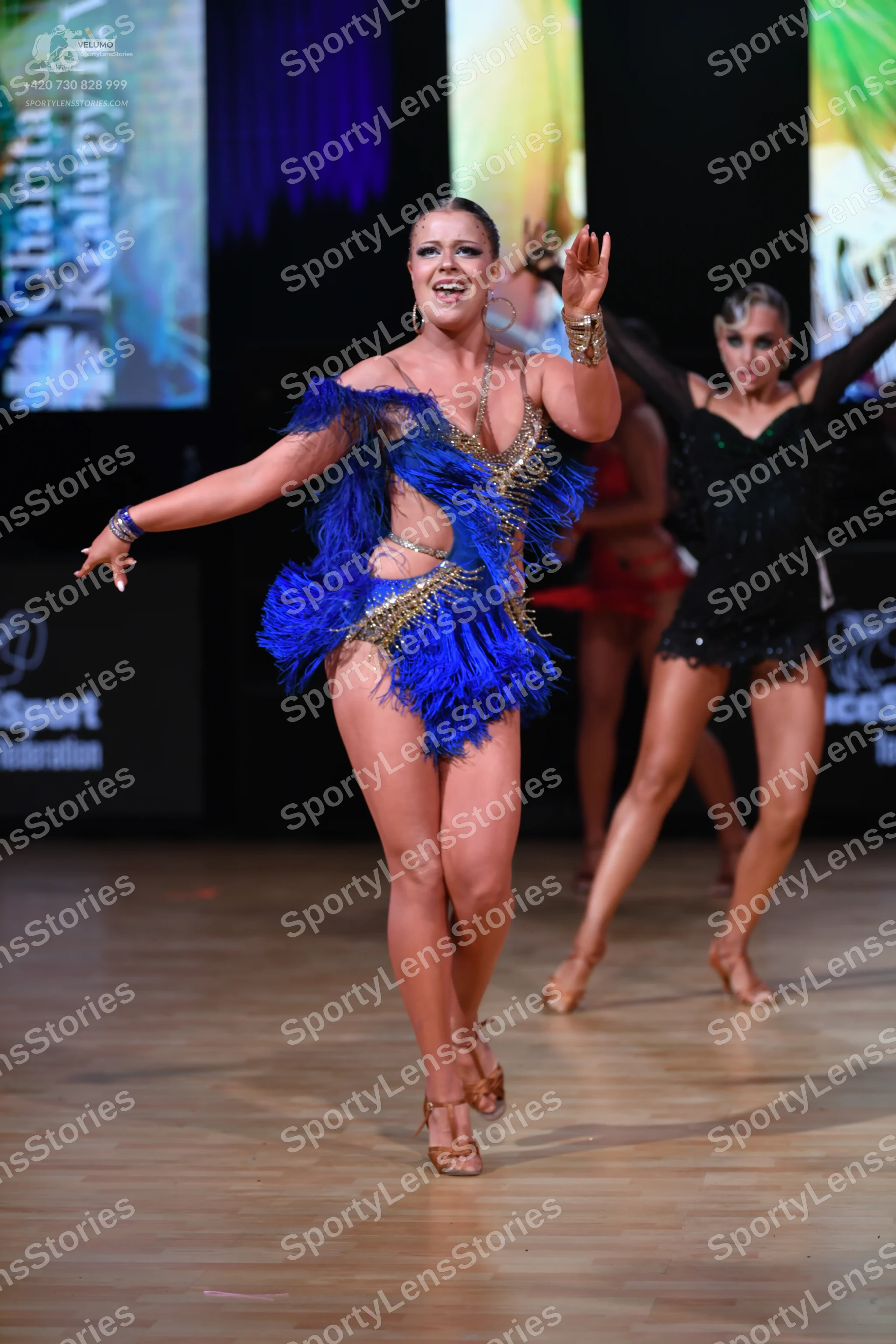 Dancesport competitor: Female dancer in foreground: blue latin dress with blue fringe and gold sequin e