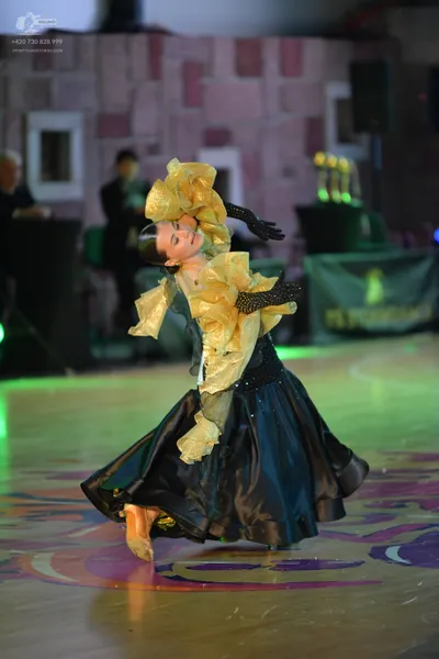 Dancesport competitor: Female dancer: black and gold ballgown with a large, ruffled gold bodice and a v