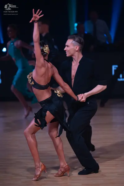 Dancesport competitor: Female dancer in foreground: black backless Latin dance costume with gold embell