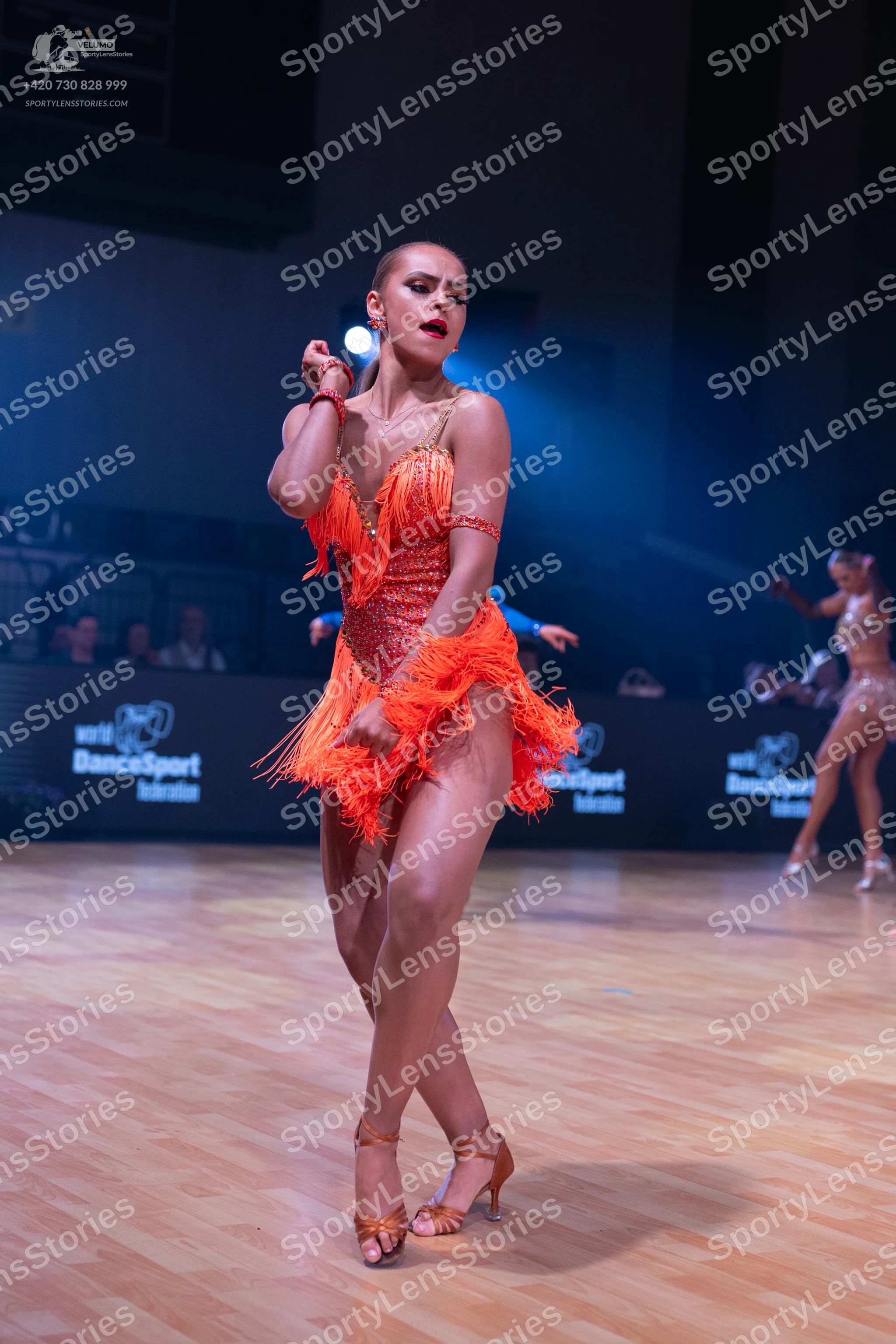 Dancesport competitor: Female dancer in foreground: orange latin dress with long fringe