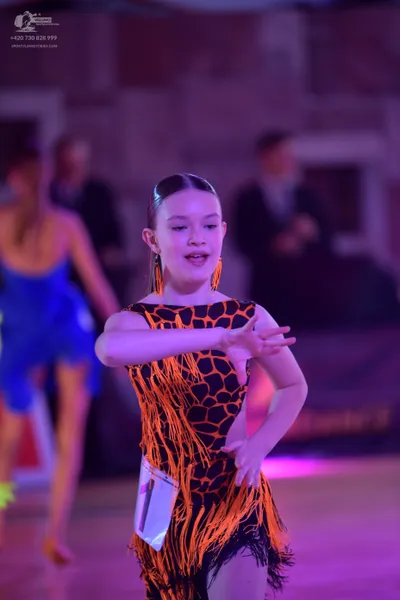 Dancesport competitor: Female dancer in foreground: black and orange animal print latin dress with long