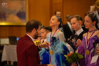 Dancesport competitor: Female dancer: blue ballgown with lace and mesh sleeves, adorned with feathers