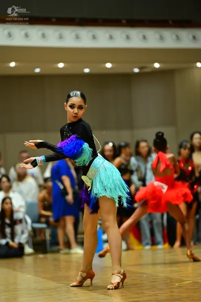 Dancesport competitor: Female dancer in foreground: black long-sleeved latin dress with vibrant multi-c