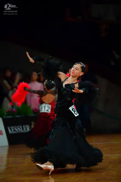 Dancesport competitor: Female dancer in foreground: black dress with large black feather or fringe trim