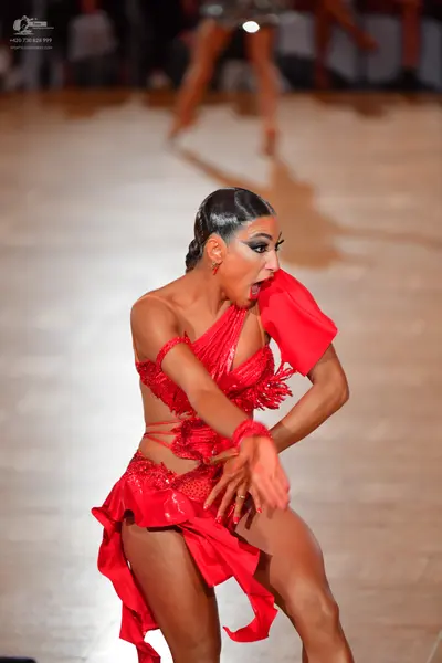 Dancesport competitor: Female dancer in foreground: red latin dress with sequins and ruffles
