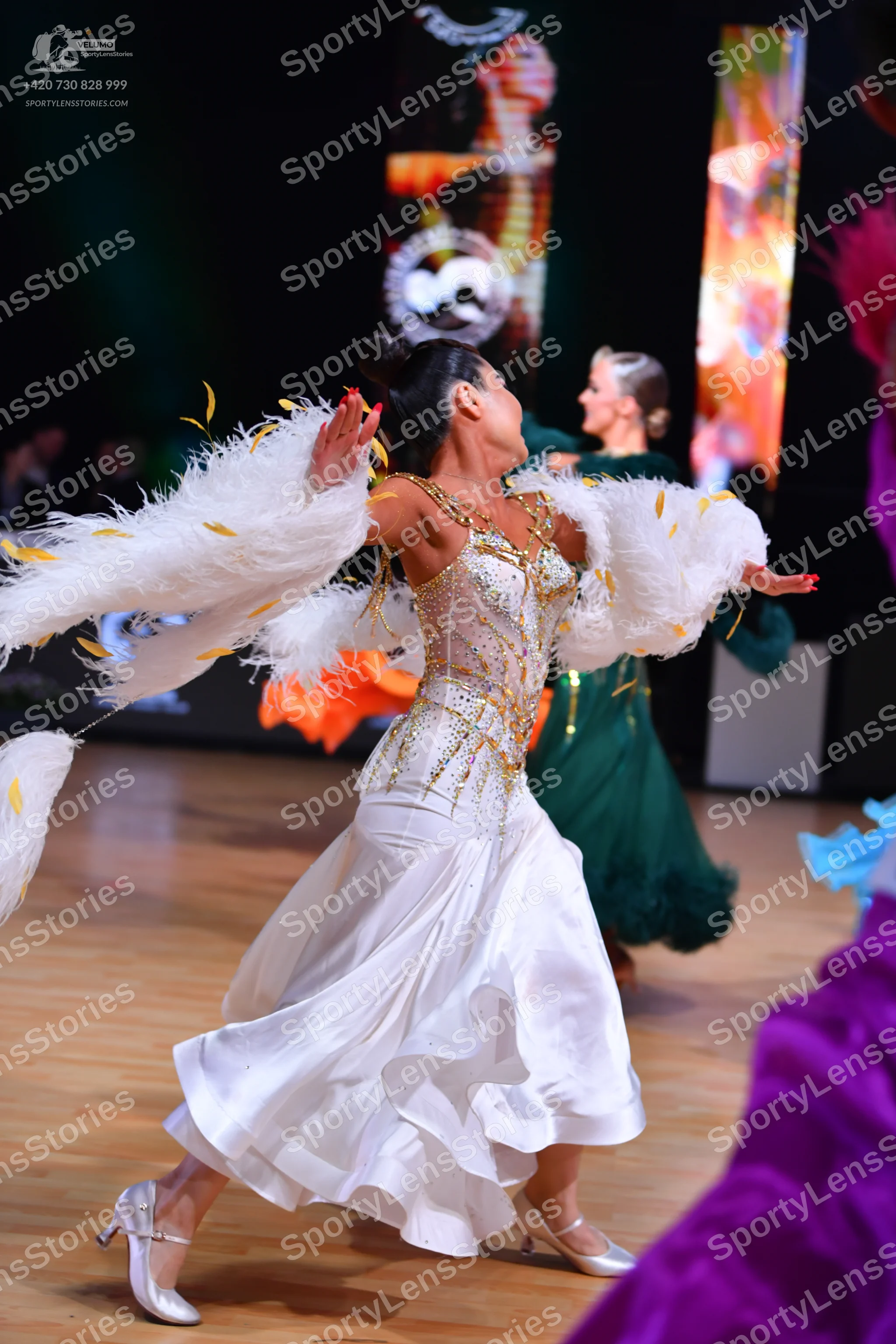 Dancesport competitor: Female dancer in foreground: white ballroom gown with a heavily embellished, seq