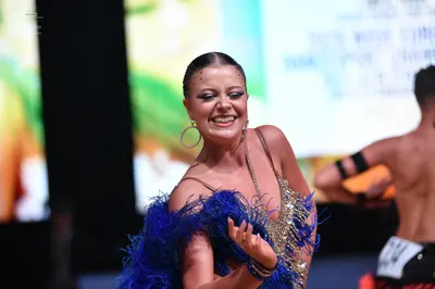 Dancesport competitor: Female dancer: gold/bronze sequined latin dress with blue feather trim and large