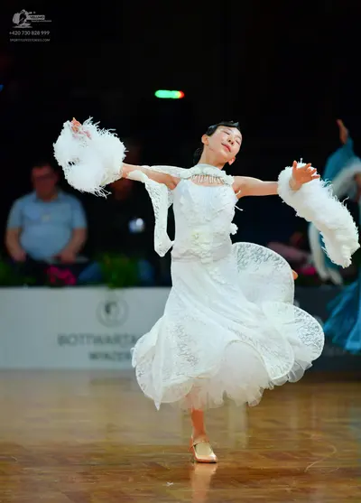 Dancesport competitor: Female dancer: white lace ballroom dress with large white fluffy arm accessories