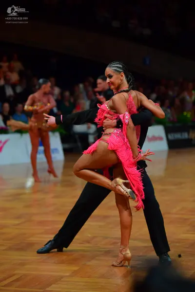 Dancesport competitor: Female foreground dancer: bright pink Latin dress with fringe and sequins