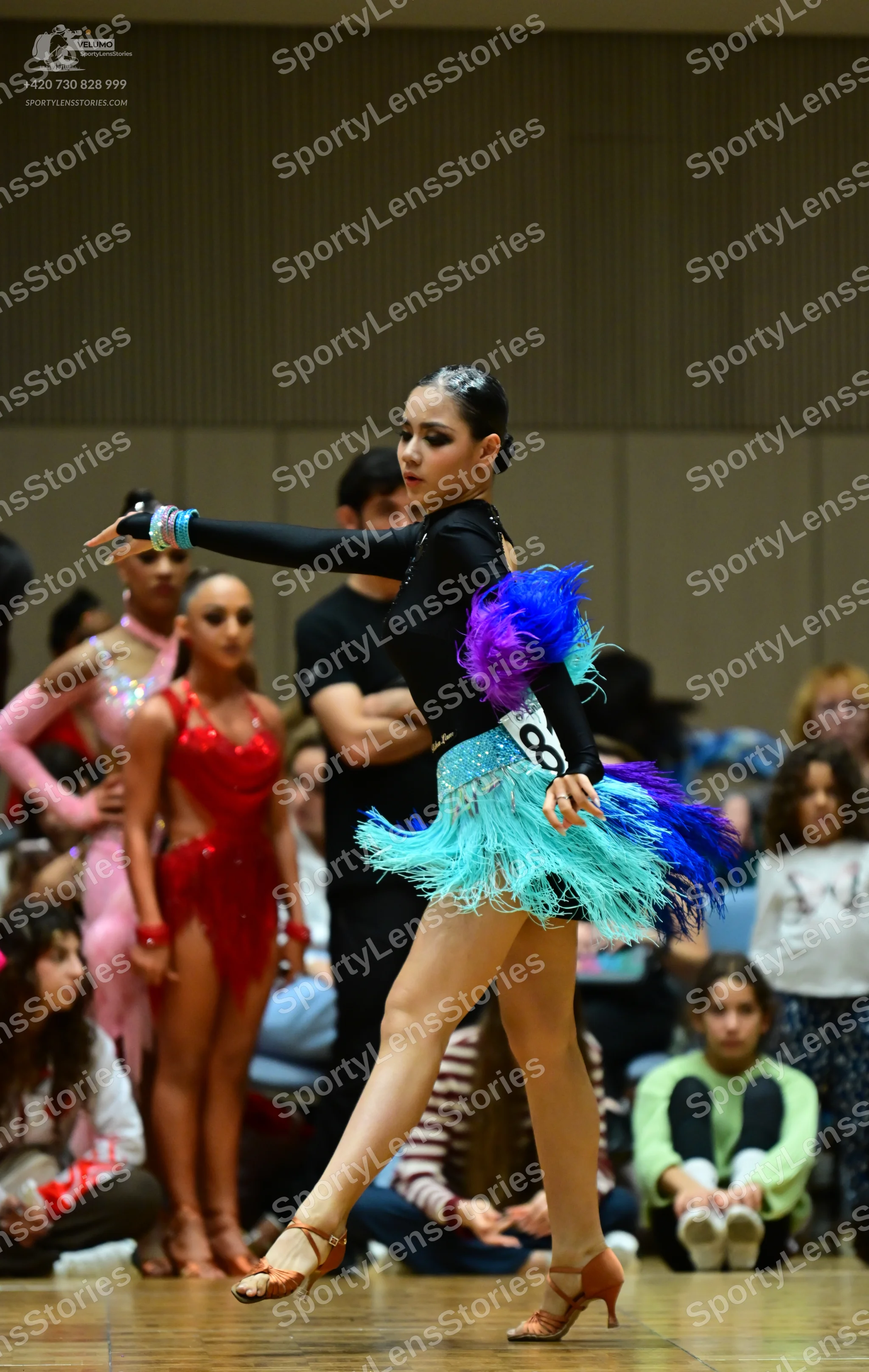 Dancesport competitor: Female dancer in foreground: black long-sleeved latin dress with teal, purple, a