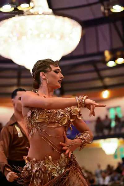 Dancesport competitor: Female dancer: gold/bronze Latin dance costume with intricate sequins, embroider
