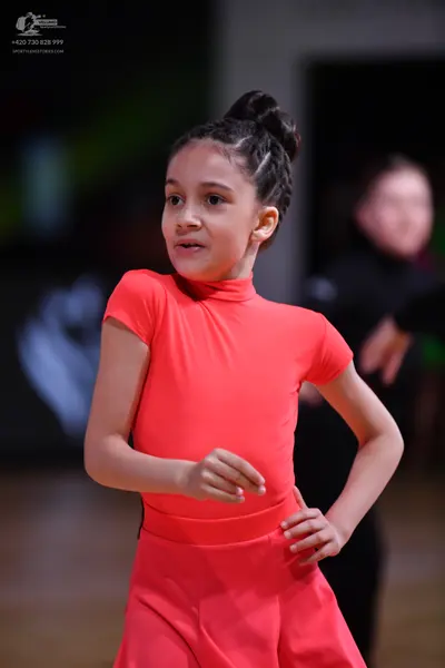 Dancesport competitor: Female dancer: bright coral-colored short-sleeved top and matching skirt in a sm