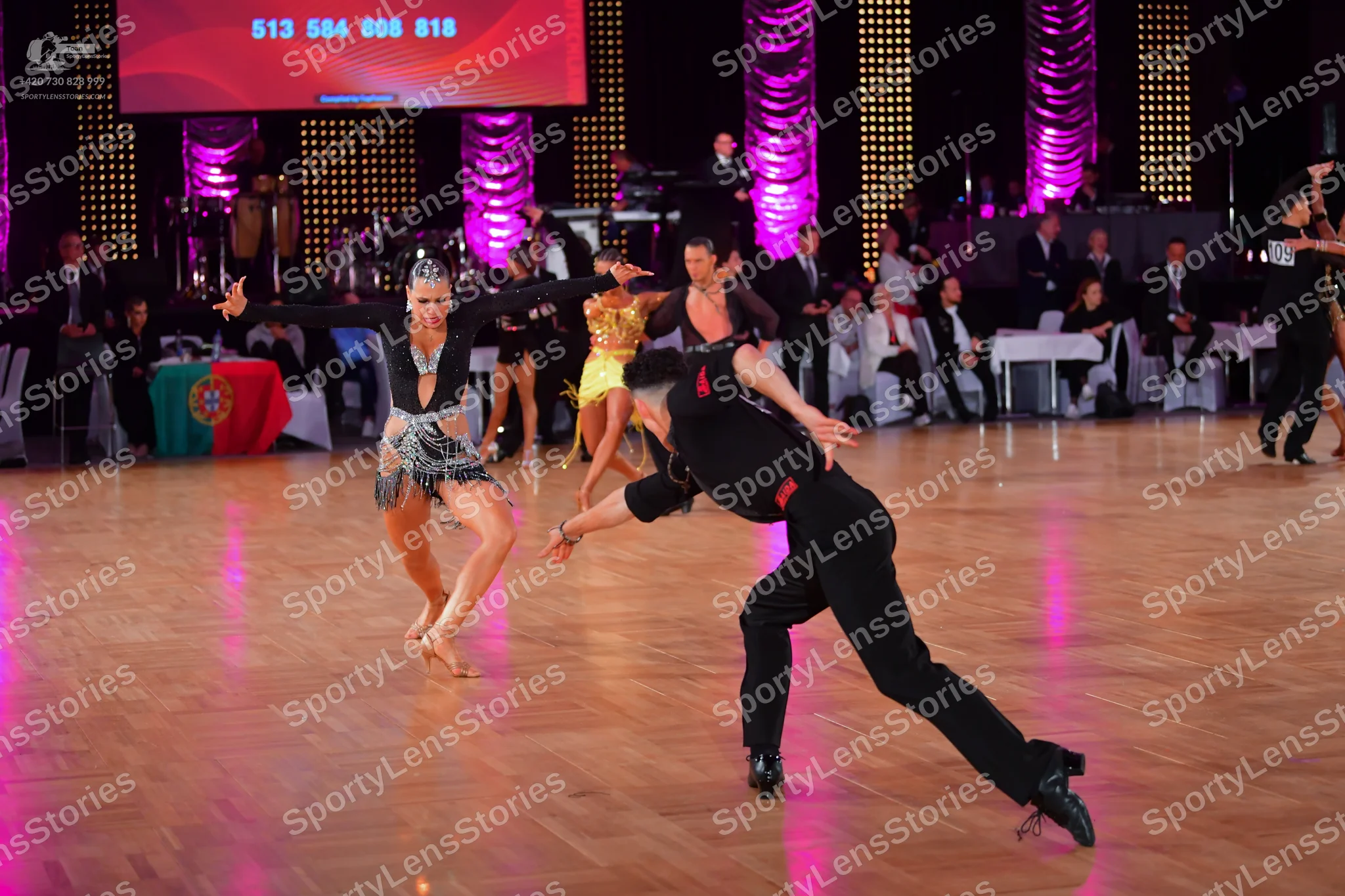 Dancesport competitor: Female dancer in foreground: black Latin dance dress with silver sequin and bead