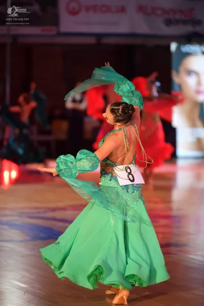 Dancesport competitor: Female dancer in foreground: large green ballgown with sheer, wavy green fabric 