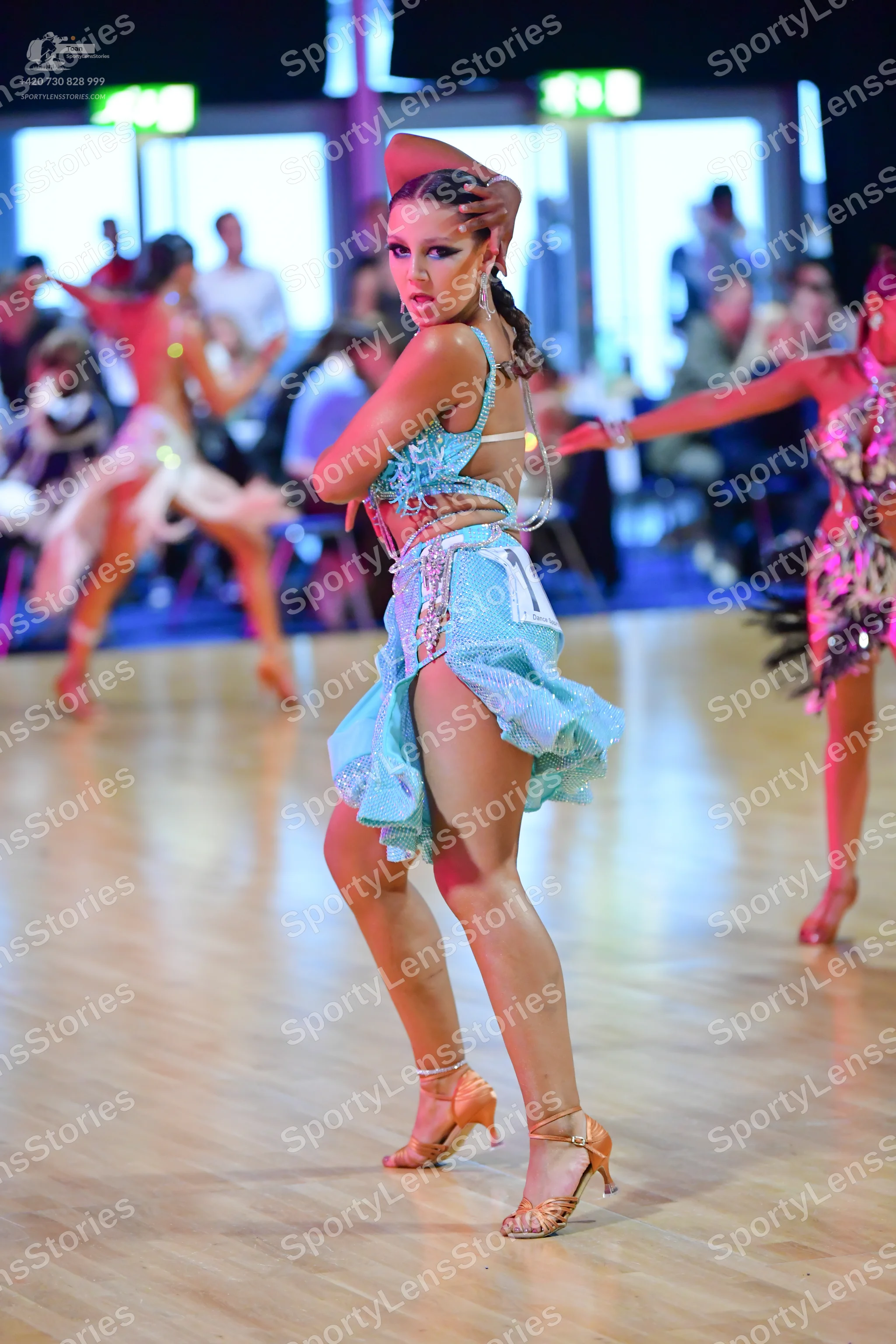 Dancesport competitor: Female dancer in foreground: light blue sequined latin dress with thin straps an