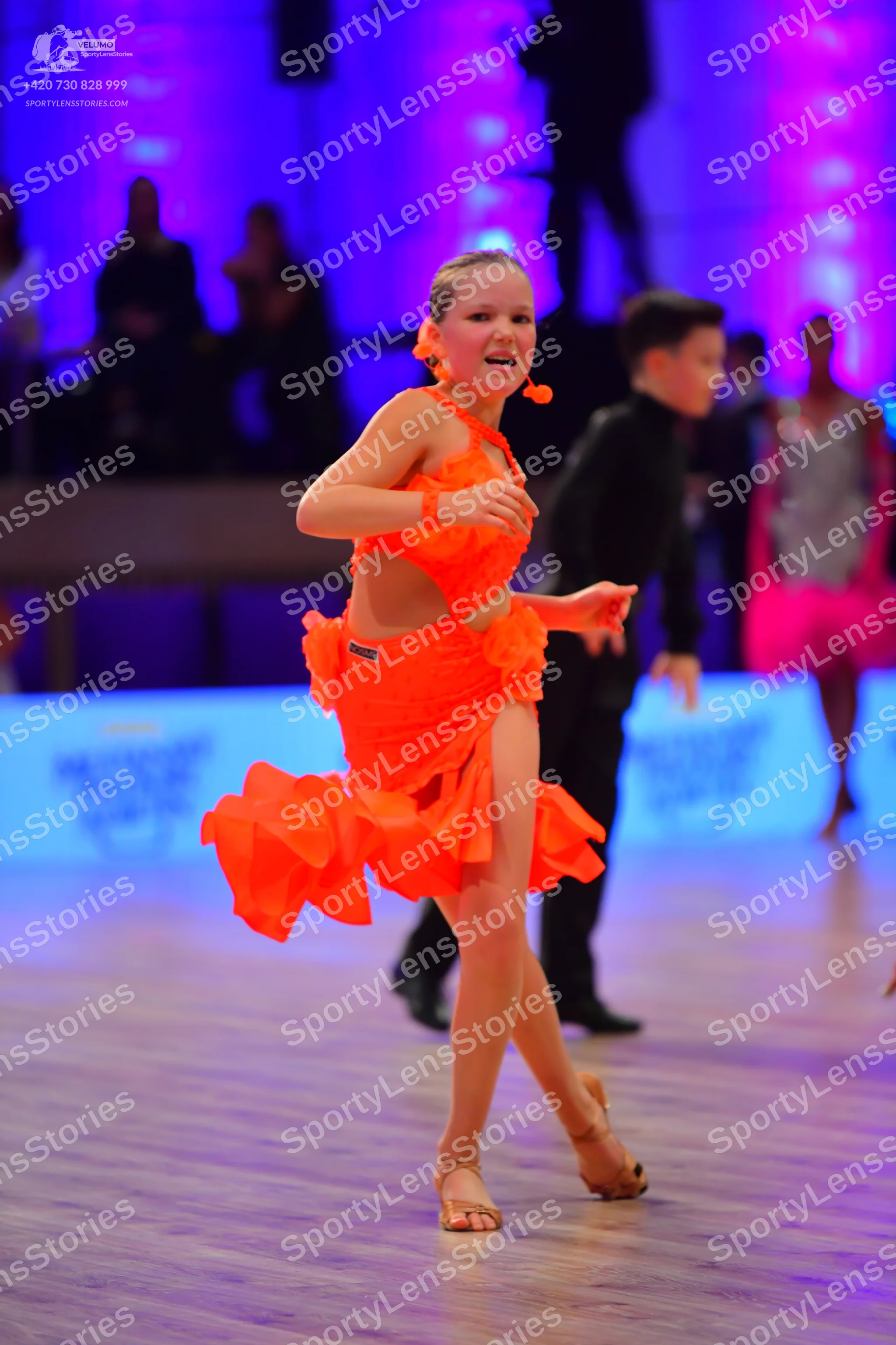 Dancesport competitor: Female dancer in foreground: orange latin dress with a ruffled, layered skirt