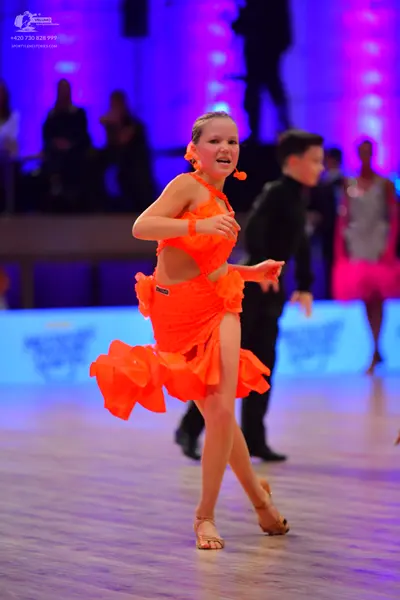 Dancesport competitor: Female dancer in foreground: orange latin dress with a ruffled, layered skirt