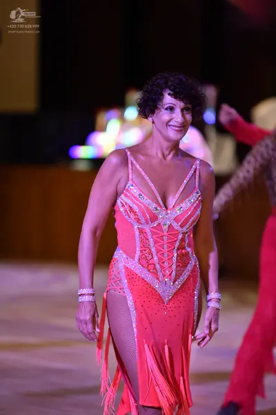 Dancesport competitor: Female dancer: bright pink/coral Latin dress with sequins, rhinestones, and frin