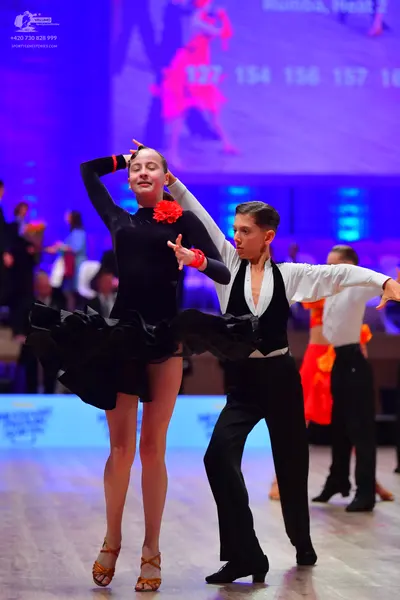 Dancesport competitor: Female dancer: black long-sleeved dress with a red flower accessory at the neckl