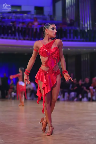 Dancesport competitor: Female dancer in foreground: red latin dress with sequins and asymmetric fabric 