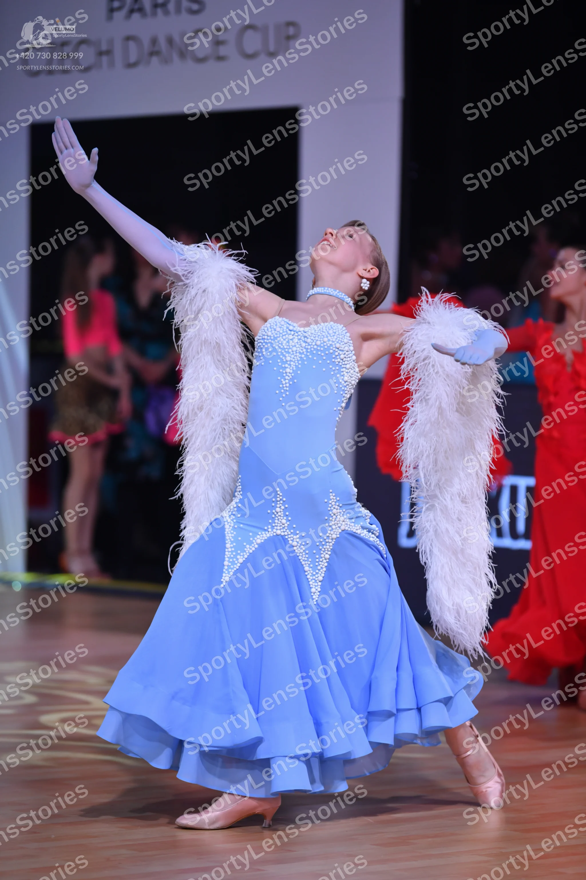 Dancesport competitor: Female dancer in foreground: light blue ballroom gown with silver-toned embellis