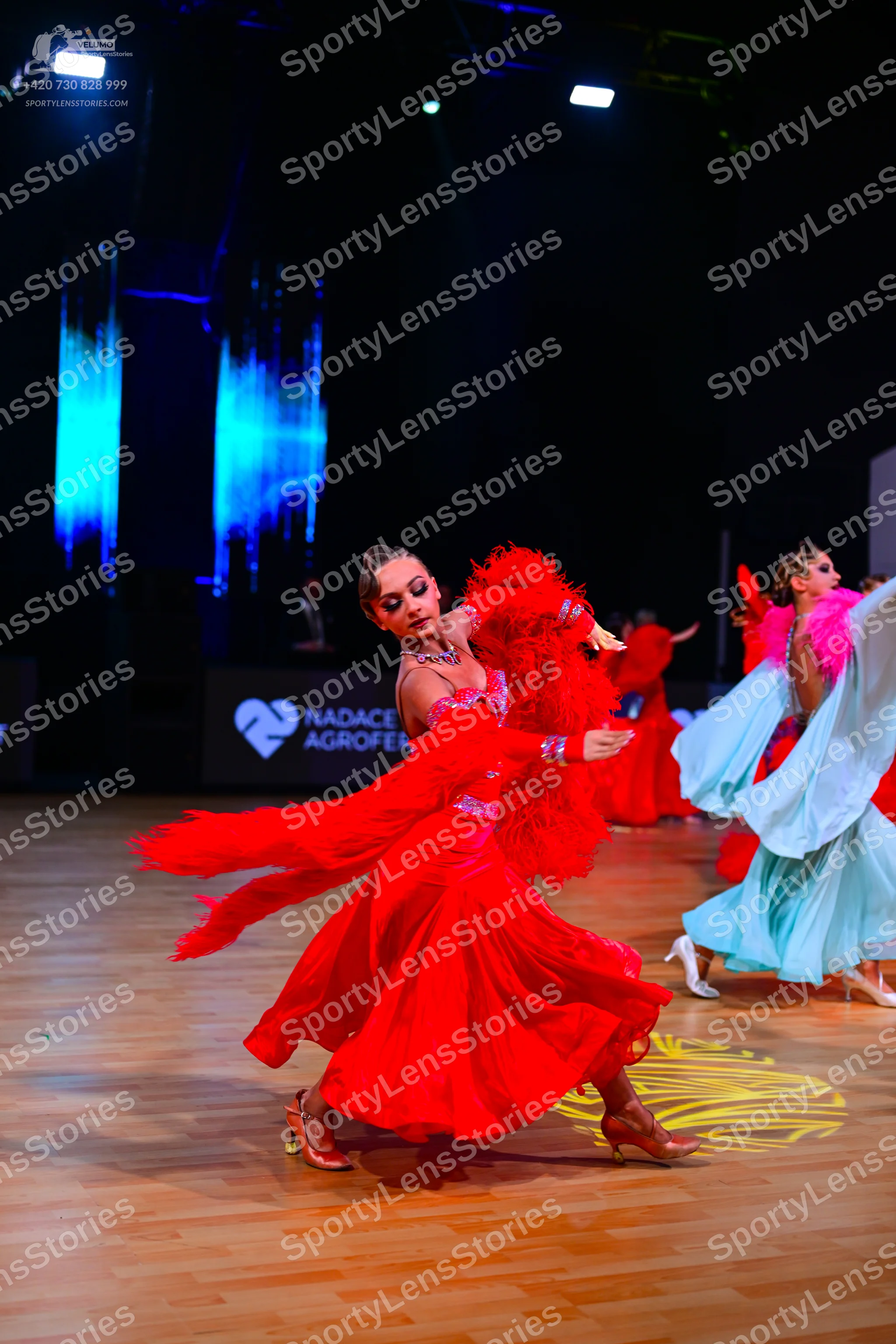 Dancesport competitor: Female dancer 1: red latin dance dress with feathered sleeves and a large, flowi