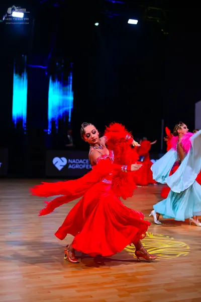 Dancesport competitor: Female dancer 1: red latin dance dress with feathered sleeves and a large, flowi